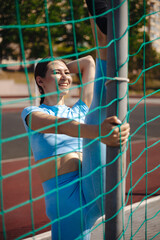 young woman doing yoga exercises and stretching in the fresh air near a green volleyball net