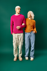 fashionable man and woman in winter outfits posing with hands in pockets on turquoise background