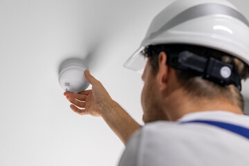 worker installing photoelectric smoke detector on house ceiling. home security and fire alarm system - obrazy, fototapety, plakaty