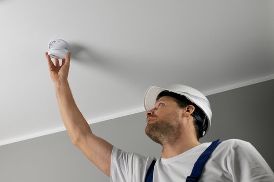 fire safety engineer installing photoelectric smoke detector on house ceiling. home security and fire alarm system