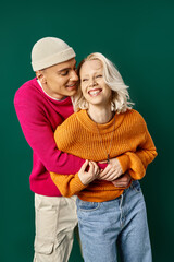 couple in winter attire having fun, man in beanie embracing happy girlfriend on turquoise backdrop