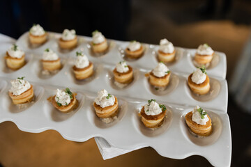 white ceramic platter with divots holding mini corn cakes with whitefish salad and chive garnish. passed appetizer at wedding cocktail hour