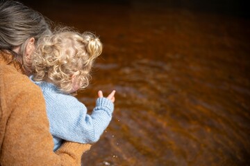 mother and baby playing on the beach. toddler in overalls walking and playing with sand