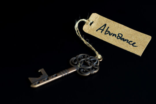 Key to abundant life concept - Old key with abundance tag isolated on black background