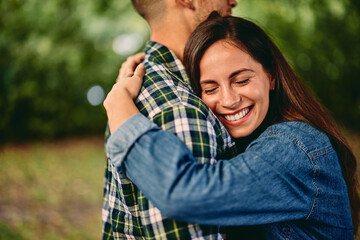 Close-up of a smiling girl, hugging her boyfriend, in nature.