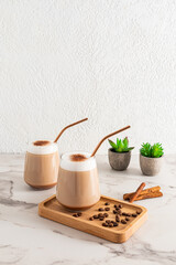 Two large glasses of cappuccino coffee or cinnamon latte on a wooden tray on a marble table with indoor plants. A delicious dessert.