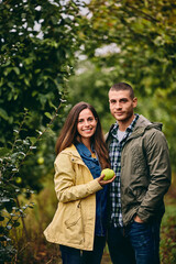 Portrait of two smiling lovers, standing in the orchard together, holding a quince.