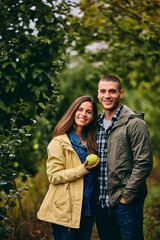 Portrait of two lovers in the orchard, posing and smiling for the camera, a girl holding a quince.