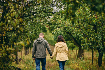 A lovely couple walking down the orchard and holding hands. Autumn season.