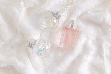 Elegant bottle of women's perfume lies on white fur among Christmas balls. Top view. A copy space. Blank bottle mockup. advertising.