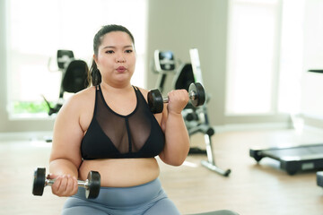 Beautiful Asian overweight woman practices lifting dumbbells with hands to build arm muscles in village gym at leisure. chubby woman intends to exercise to lose weight. Lifestyle and exercise concepts