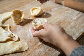 Woman making dumplings and sprinkling the flour on the top with a wooden board and roller in the background.