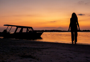 Silhouette of woman against tropical sunset at the beach by the fishing boat at the ocean