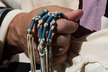 An Orthodox, Jewish man holds blue techelet tzitzit strings while reciting the Shema Yisrael during...
