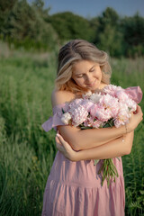 Fototapeta premium Natural cosmetics for skin care. Lovely blonde in dress stands with bouquet of peonies in nature.