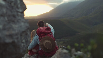 Hiking, mountain and view, couple relax on outdoor adventure and peace in nature with romance from back. Trekking, rock climbing and love, man and woman with sunset horizon sitting on cliff together.