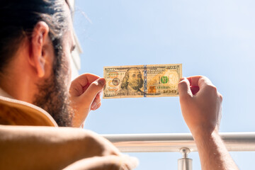 A man checks the authenticity of a hundred dollar bill by shining a light from a window. One...