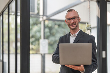 Successful businessman standing in modern office Use a laptop computer Organization or financial manager who is successful in planning investment projects