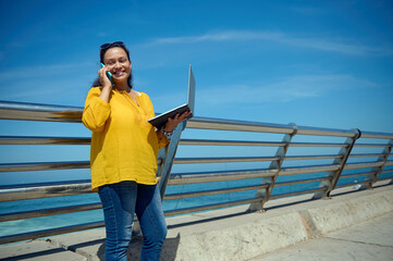 Confident multitasking sales manager holds a laptop, online works and smiles while a conversation...