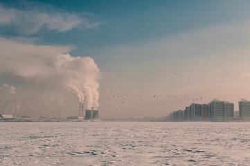 Winter landscape with snow covered frozen ice, city and pipes with thick steam