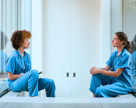 Two Female Doctors Wearing Scrubs Taking A Break In Modern Hospital