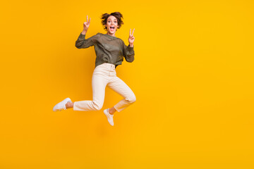 Photo of glad glamour girl dressed styishl clothes jumping up showing v-sign empty space isolated on vivid yellow color background