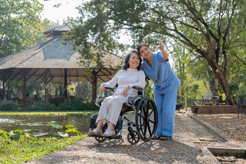Happy nurse and elderly woman sitting in wheelchair enjoying outdoor. Beautiful nurse with senior woman in wheelchair at outdoor park. Smiling disabled old lady in wheelchair at park.