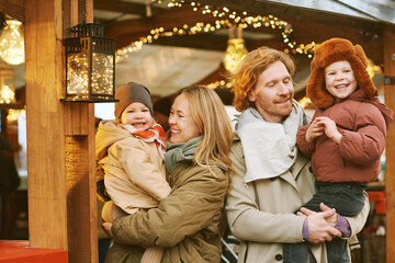 Obraz na płótnie Canvas Outdoor portrait of happy young family at Christmas market, parents with 2 little children enjoying holidays, travel with kids