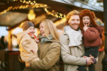 Outdoor portrait of happy young family at Christmas market, parents with 2 little children enjoying holidays, travel with kids