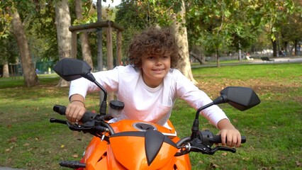 Fototapeta na wymiar Boy child 9 years old rids a big orange motorbike of his father and dreams to drive in the street like the adults - fun in childhood and the desire to grow up
