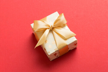 wrapped Christmas or other holiday handmade present in white paper with gold ribbon on colored background. Present box, decoration of gift on colored table, top view with copy space
