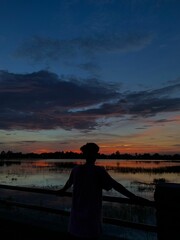 Fototapeta premium a woman standing next to a fence with the sunset behind her