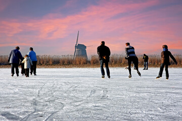Ice skating at the windmill in the countryside from the Netherlands at sunset