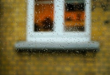 Abstraktes Motiv mit Regentropfenmuster auf Glasscheibe vor Hausfassade mit gelben Backsteinen und...