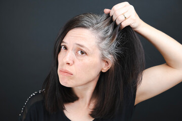 A young woman examines the gray hair on her head in a mirror on a black background. Close up texture of gray hair.