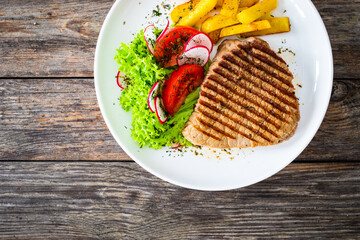 Grilled beef steak with fresh vegetable salad and French fries on wooden table
