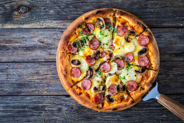 Circle pizza with sausages, onion and mozzarella cheese on wooden table
