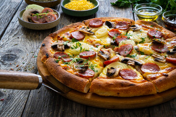 Circle pizza with sausages, onion and mozzarella cheese on wooden table
