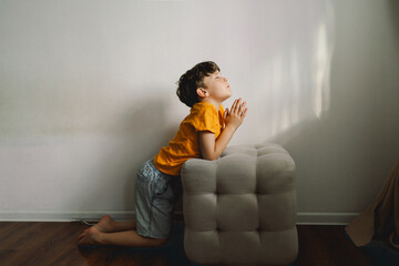A boy in an orange T-shirt prays at home. Reading the Holy Bible. Concept for faith, spirituality...
