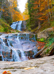 A beautiful waterfall with multiple cascades during autumn with fallen leaves around.