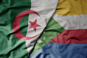 big waving national colorful flag of algeria and national flag of comoros .