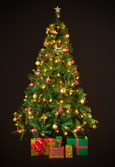 Beautifully decorated Christmas tree on a black background. Boxes with gifts lie under the Christmas tree.
