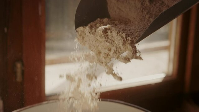 Close-up of fresh white flour in a measuring scoop.  Slow-motion falling flour. Baking ingredients. Traditional concept of flour production. 
