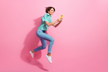 Fototapeta na wymiar Full size profile portrait of energetic sportive girl jump run use smart phone empty space isolated on pink color background