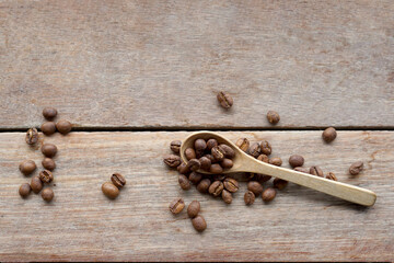 Roasted coffee beans in wooden spoon and spread on wooden table background. It is a medium roast with medium intensity coffee flavor. Slightly sweet and sour, suitable for both hot and cold coffee. 