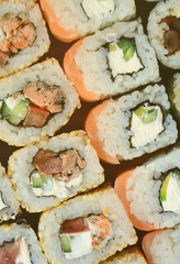 Close-up of a lot of sushi rolls with different fillings lie on a wooden surface. Macro shot of cooked classic Japanese food with a copy space.