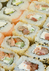 Close-up of a lot of sushi rolls with different fillings lie on a wooden surface. Macro shot of cooked classic Japanese food with a copy space.