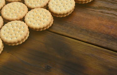 A round sandwich cookie with coconut filling lies in large quantities on a brown wooden surface. Photo of edible treats on a wooden background with copy space