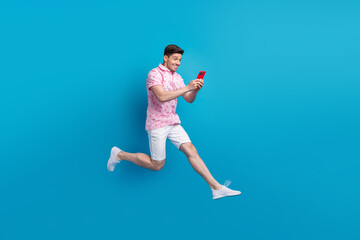Fototapeta na wymiar Full body profile photo of crazy cheerful man jump rush use smart phone texting isolated on blue color background