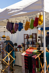 Colorful woven yarn cloth displayed for sale on a wooden rack at a local farmers market - scarves, mittens, and hats